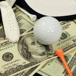 Golf ball and tee on stack of money.