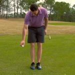 A golfer drop's a golf ball at his knees.