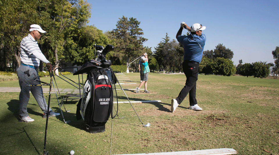 Mexican golf star José de Jesús Rodriguez (R)  practices on the driving range at the Club de Golf Santa Margarita, located in Irapuato, Mexico, while being observed by his brother, Rosendo Rodriguez Martinez, 42, a golf coach (L). Rodriguez lived near the club as a child and began working there as a caddy, before his exceptional life trajectory transformed him into the golf legend he is now. 
note: young boy in background is Marcelo León Batta, 8, who appears in other photos.