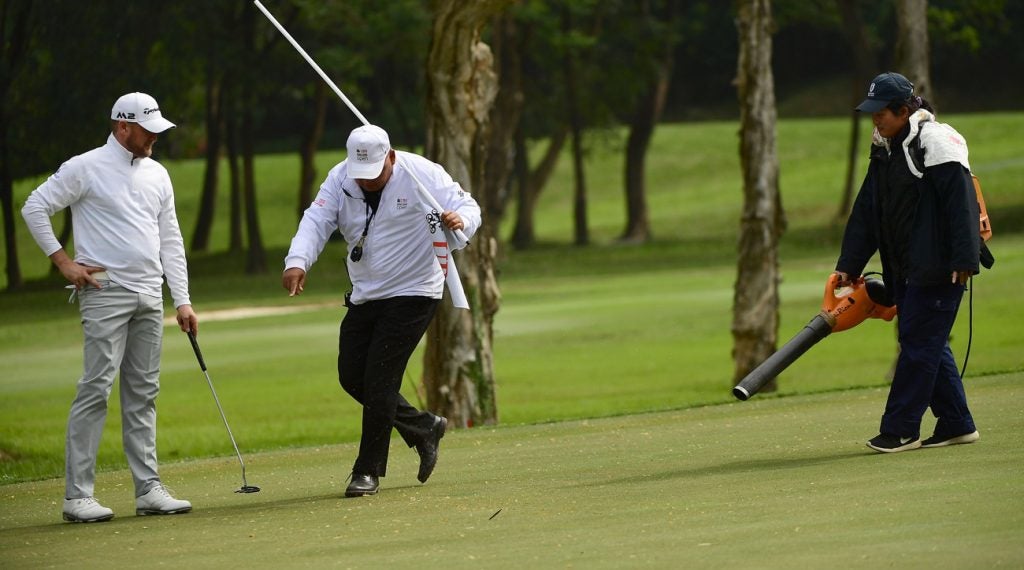 An Asian tournament director shows a worker where to direct his blower on the green.