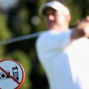 Golfer in backswing with "no phones or cameras" sign in background