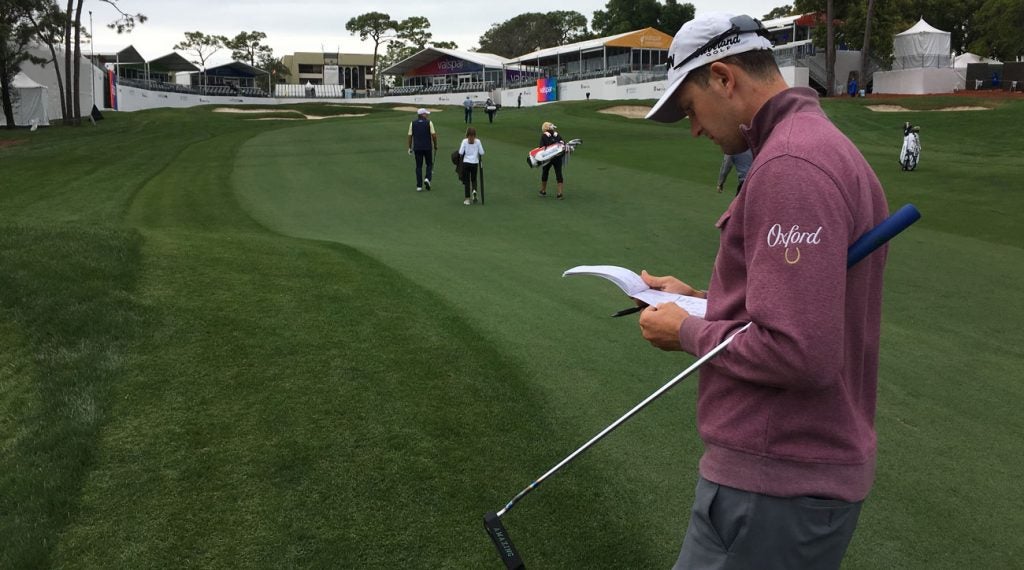 Trainer consults his yardage book at the Valspar Championship, with Steve Stricker and his wife and daughter in the background.