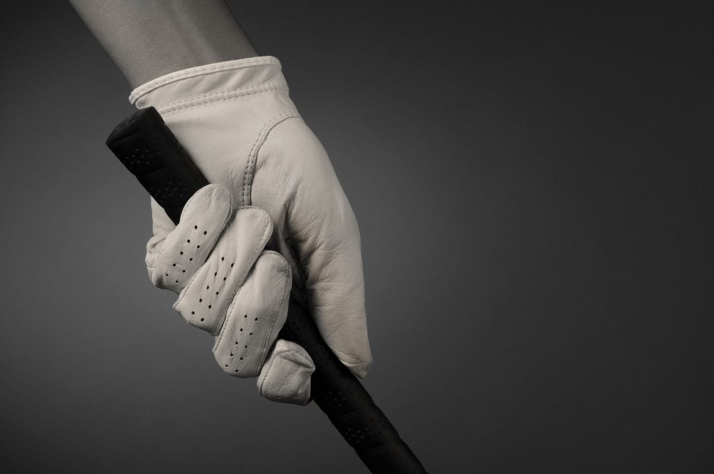 Closeup of a golfers hand on the handle of a golf club.