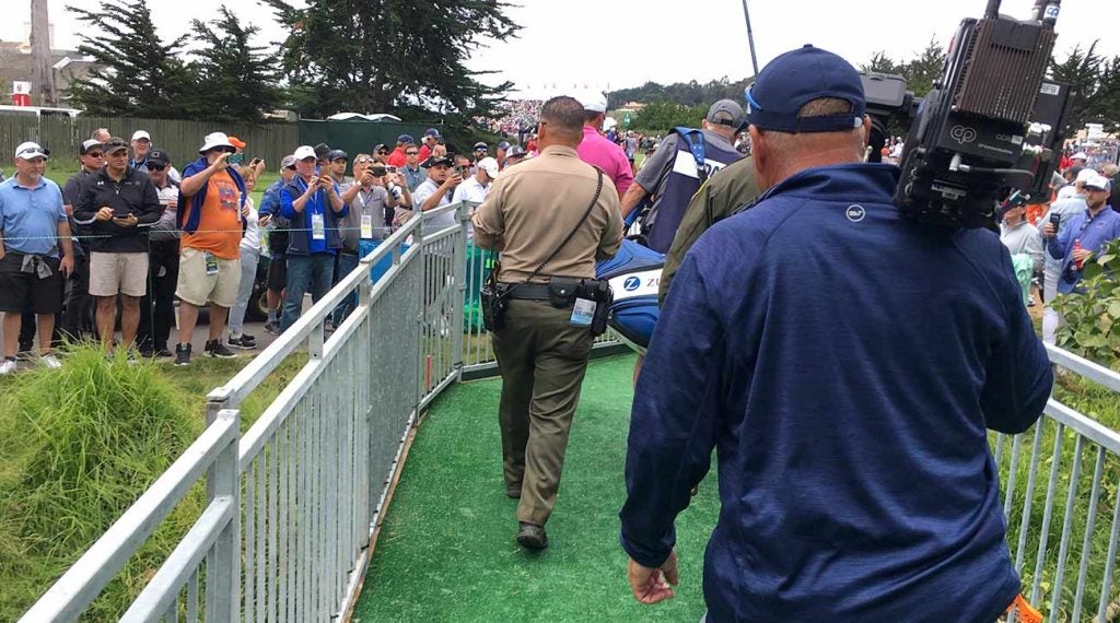 Officer Arroyos walks behind Jason Day and caddie Steve Williams (and in front of a cameraman) on his way to the 17th tee box on Thursday at Pebble Beach.