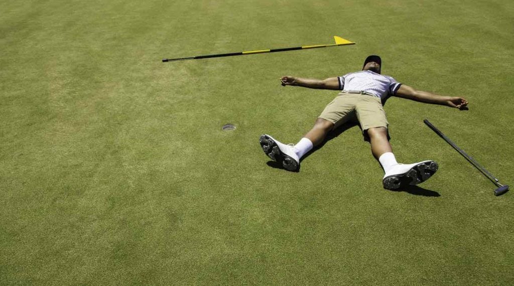 Golfer lying on putting green with his arms and legs open wide feeling exhausted.
