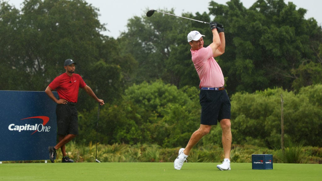 Peyton Manning hits a tee shot as Tiger Woods watches on