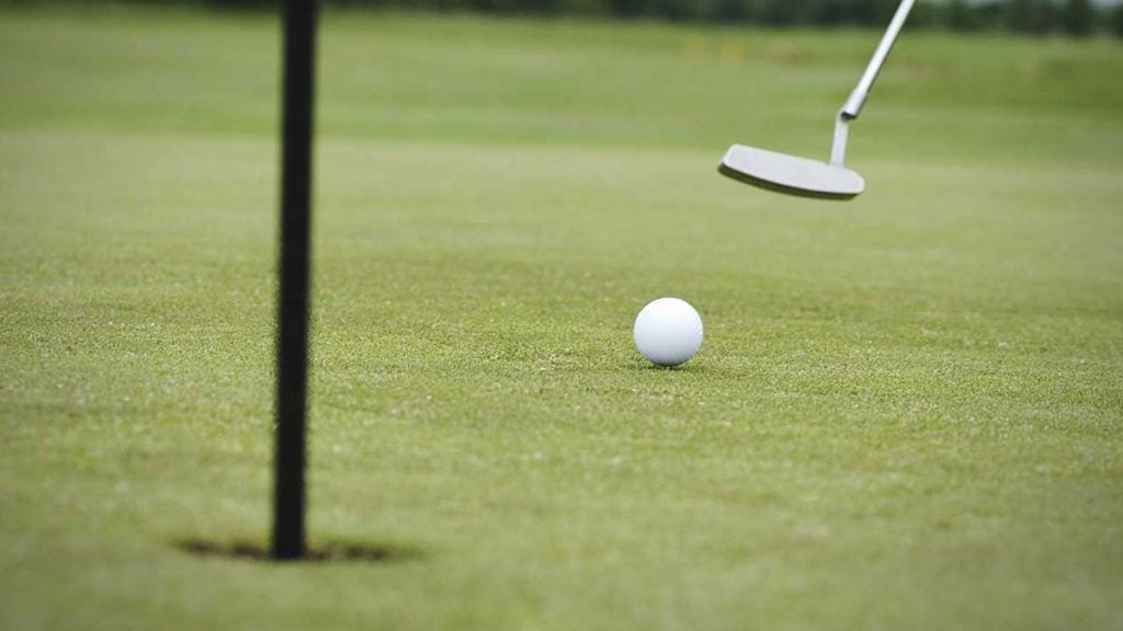 A golfer rolls a putt toward the hole