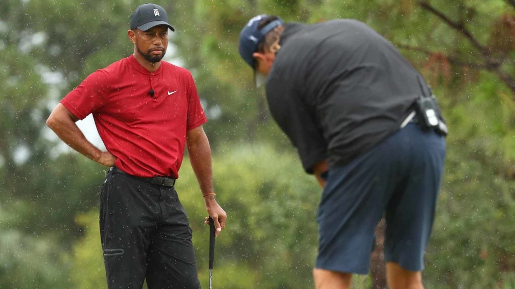Tiger Woods watches Phil Mickelson putt on golf green