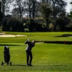 man swings tee shot golf course