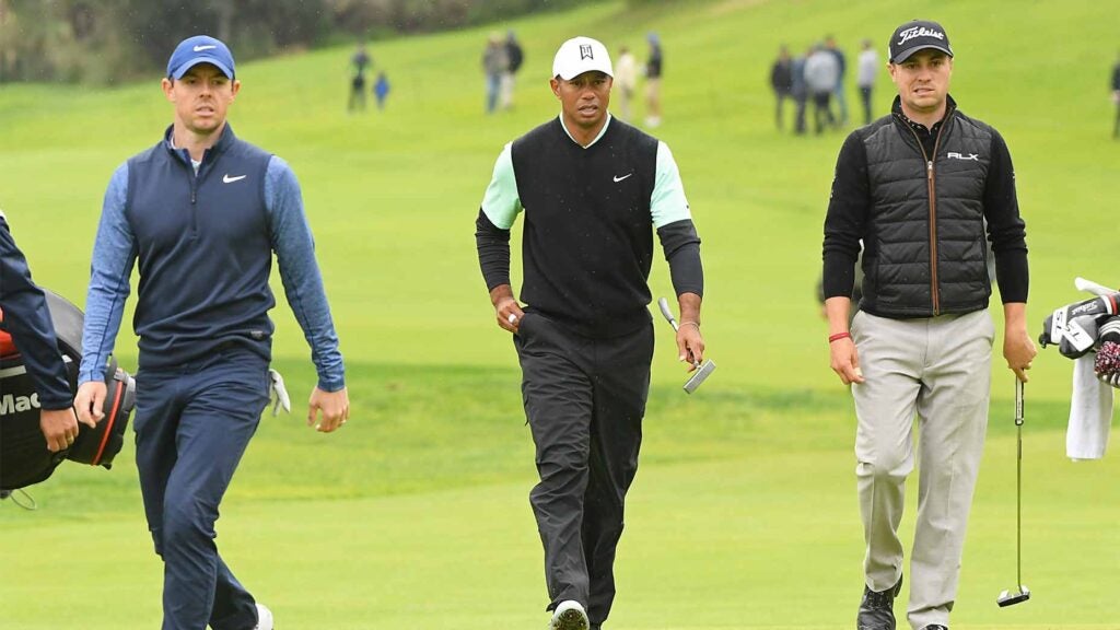 Rory McIlroy, Tiger Woods and Justin Thomas walk down the fairway.