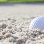 golf ball sits in sand bunker on golf course