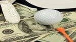 A golf ball, golf glove,and golf tee sit on a pile of U.S. dollars