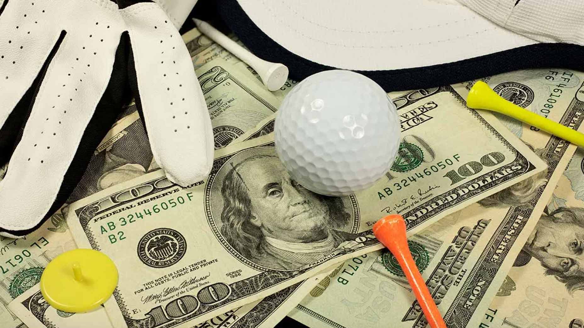 A golf ball, golf glove, and golf tee sit on a pile of US dollars