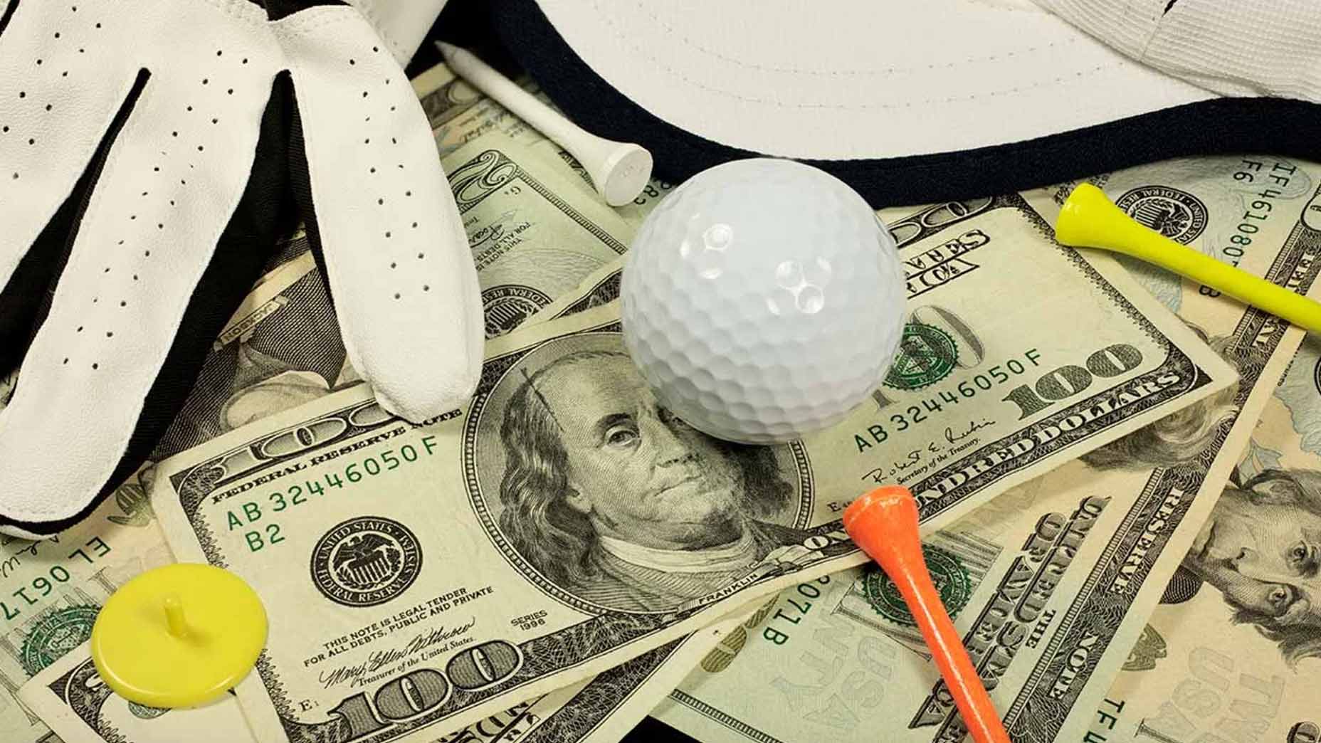 A golf ball, golf glove,and golf tee sit on a pile of U.S. dollars