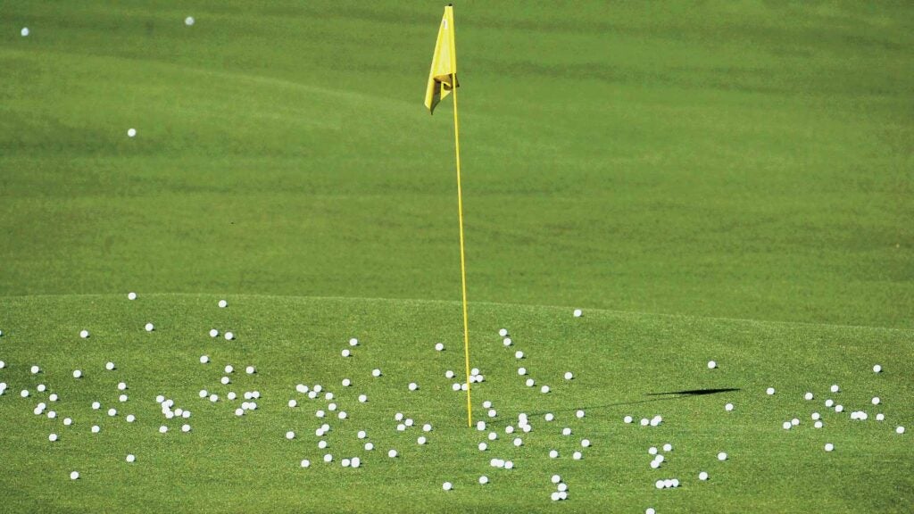 Golf practice balls sit on a practice green around a yellow flagstick