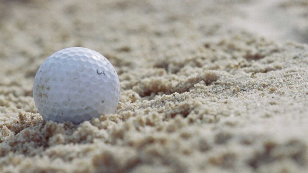 A golf ball rests in the sand on a hole.
