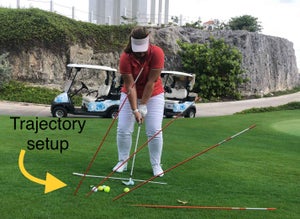 A golfer uses alignment sticks to practice different chipping trajectories
