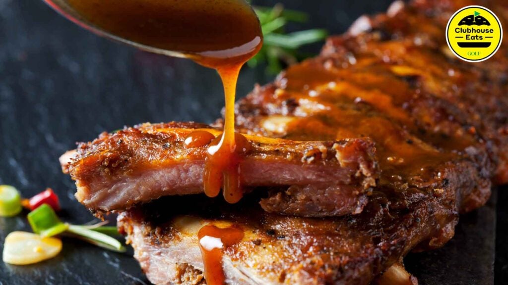 a spoon of barbecue sauce dripping on a platter of spare ribs
