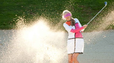 a woman hits a big splash of sand in a bunker