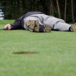 golfer lying down on green with ball near hole in foreground