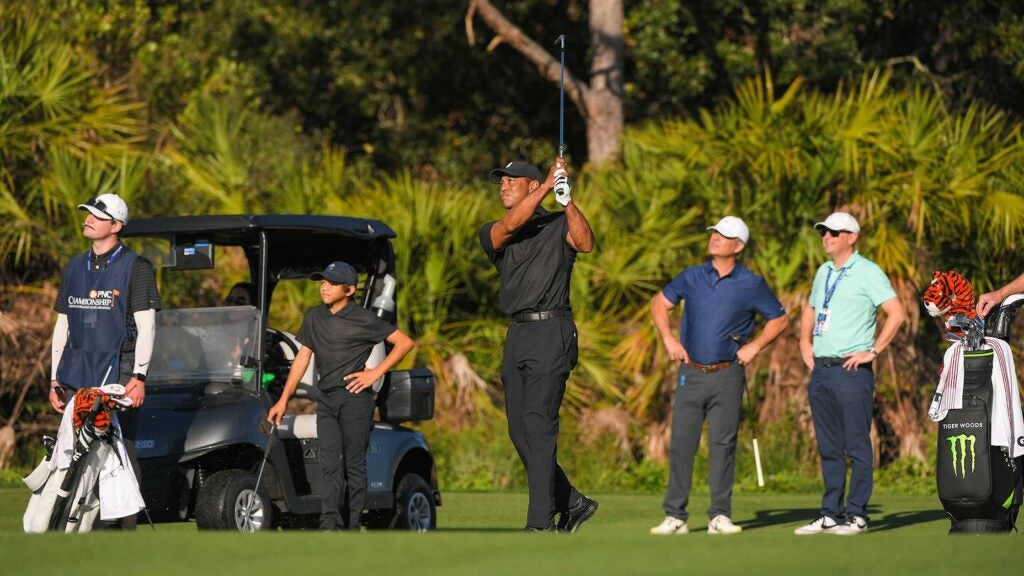 Tiger Woods hit a shot as Charlie Woods and caddie Joe LaCava Jr. (left) look on.