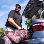 A golfer takes their bag of their car.