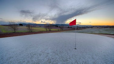 Golf green covered in snow with red flagstick