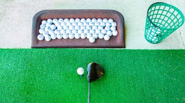 golf driver rests on driving range with practice golf ballsmat