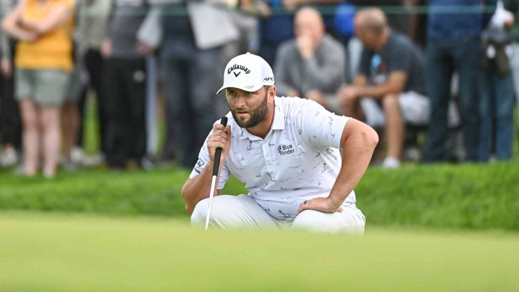 Jon Rahm crouches to read putt on green during 2022 Farmers Insurance Open