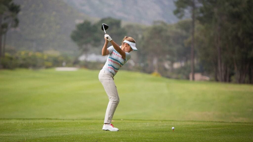 A young blond woman stands on the tee box and hits her driver