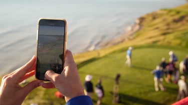 a person is holding a mobile phone while watching golf