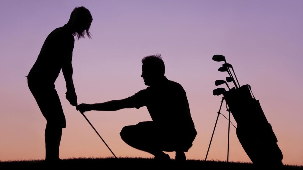 A silhouette of a woman getting a golf lesson from a golf professional and instructor.