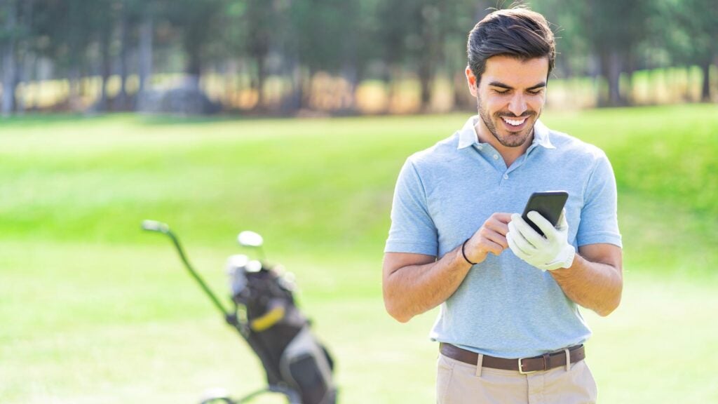 Smiling golfer talking on his mobile phone on the course standing next to his bag with golf clubs.