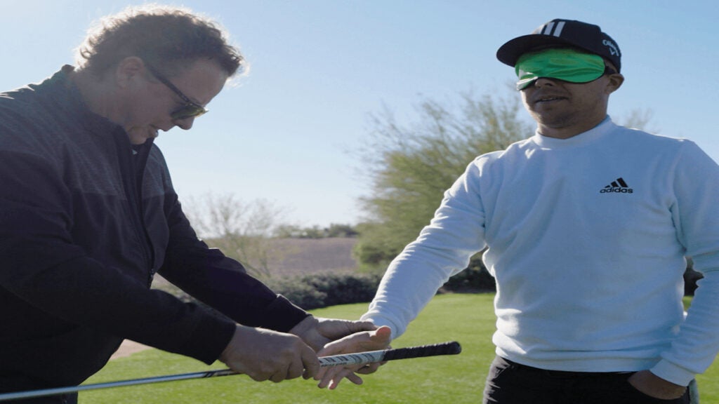 Xander Schauffele getting assistance while playing a par-3 blindfolded