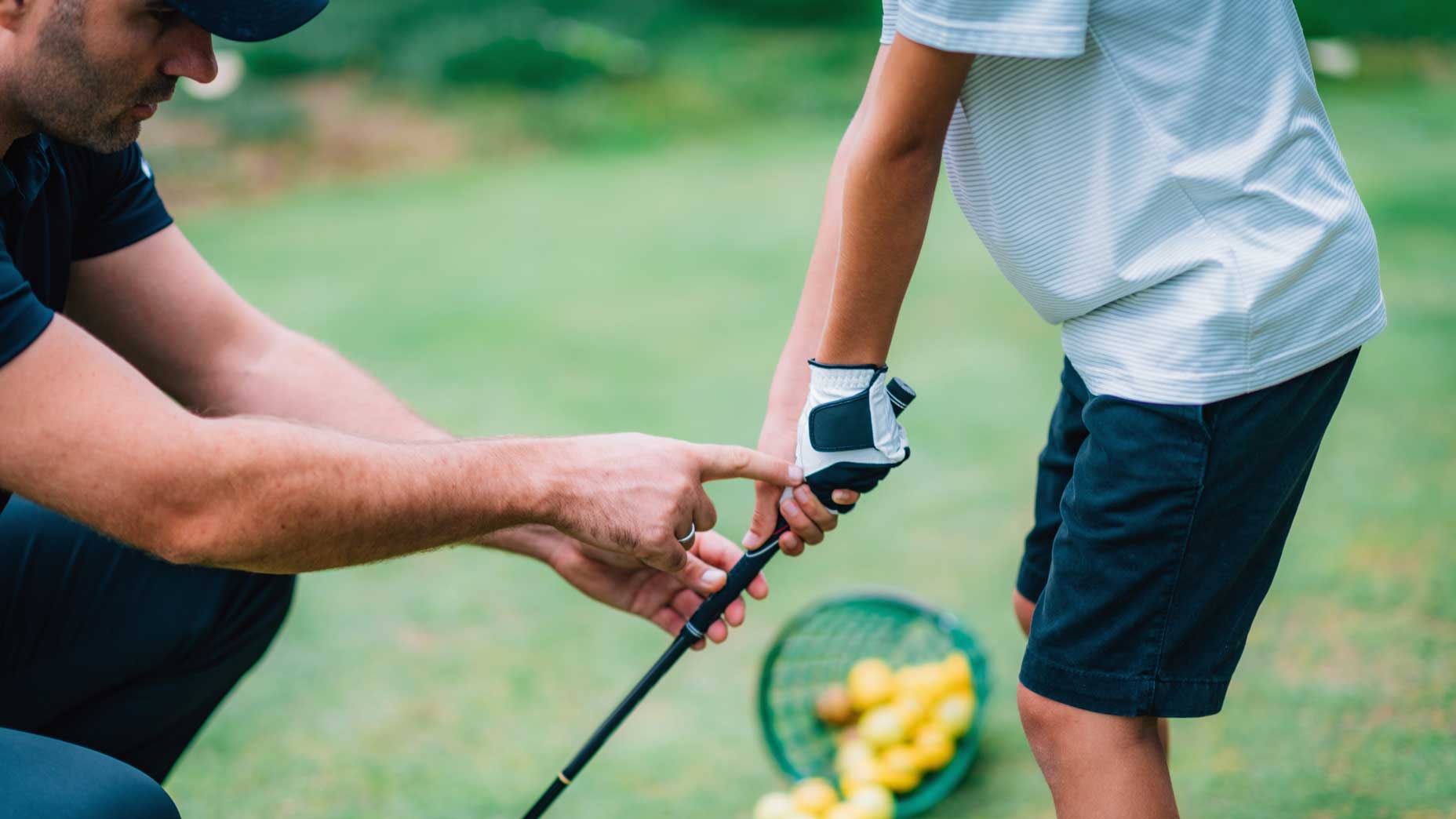 Golf Instructor adjusting young boy’s grip