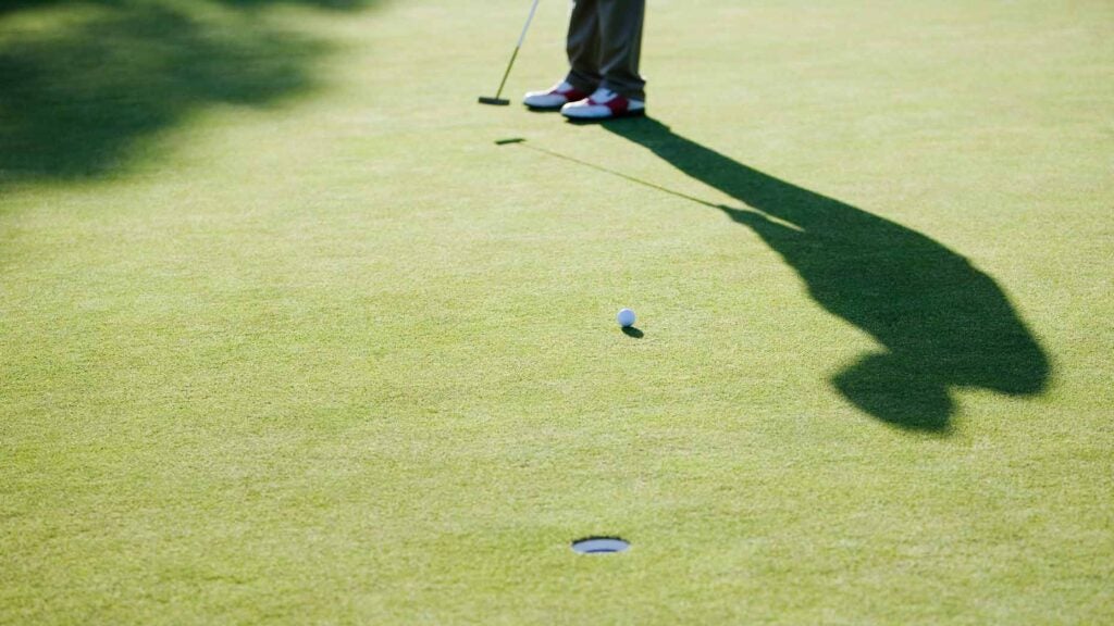 golfer hits putt on green with shadow casting