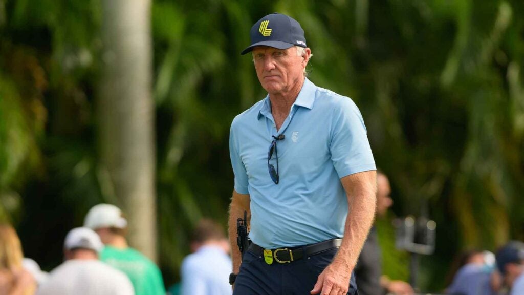 greg norman walks at LIV Miami in a blue shirt and navy hat