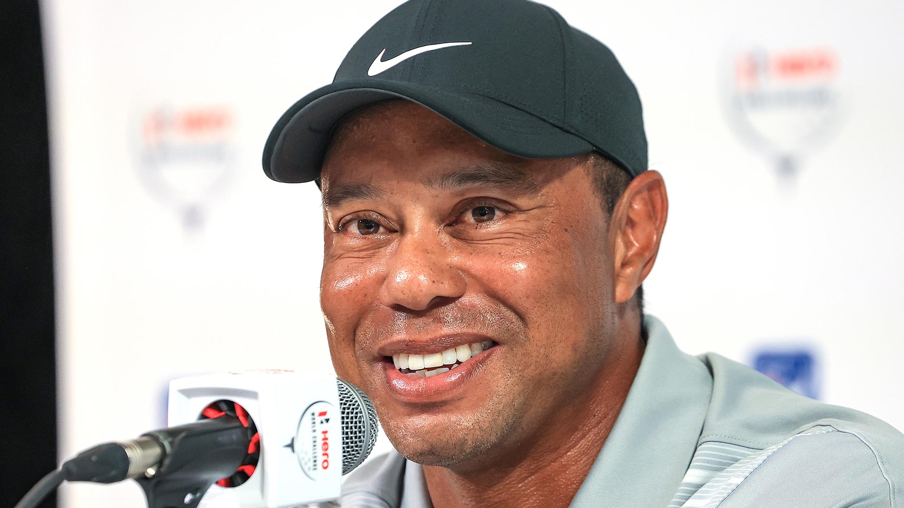 Tiger Woods smiles from the podium at the Hero World Challenge in front of the microphone