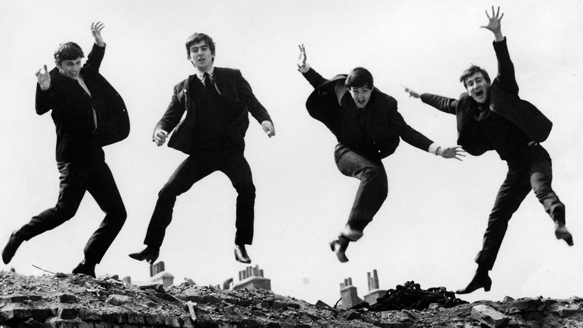 john lennon, paul mccartney, ringo star and george harrison jump off a brick wall in suits