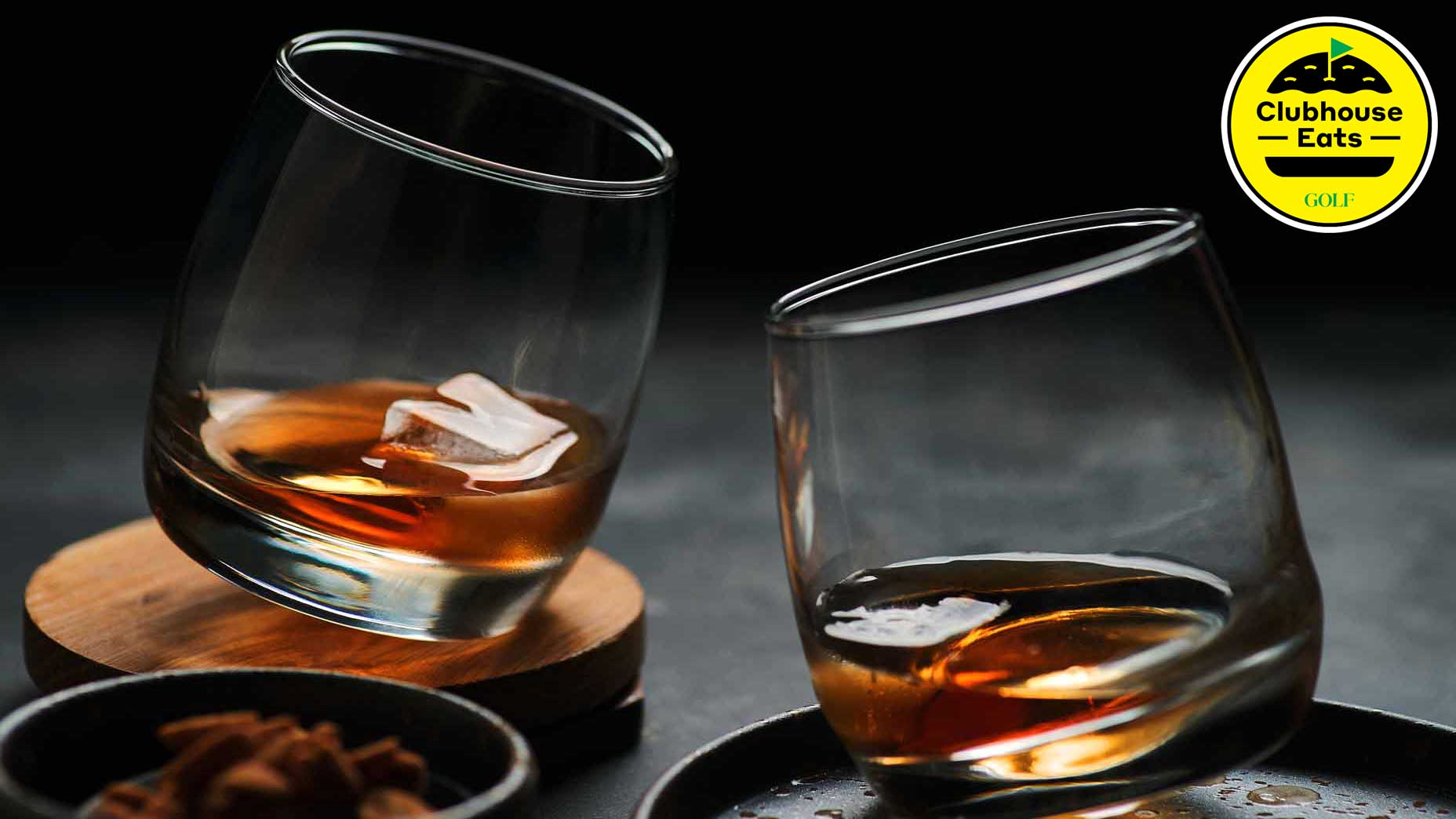 Two glasses of bourbon on the rocks clinking together on black background