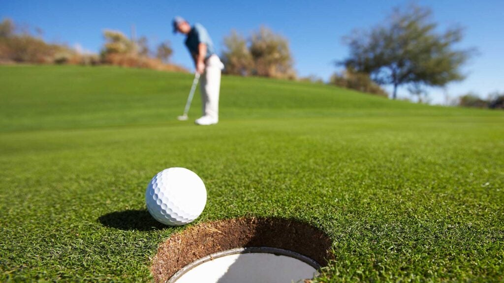 Golf ball sits on edge of cup on golf green after golfer putted it