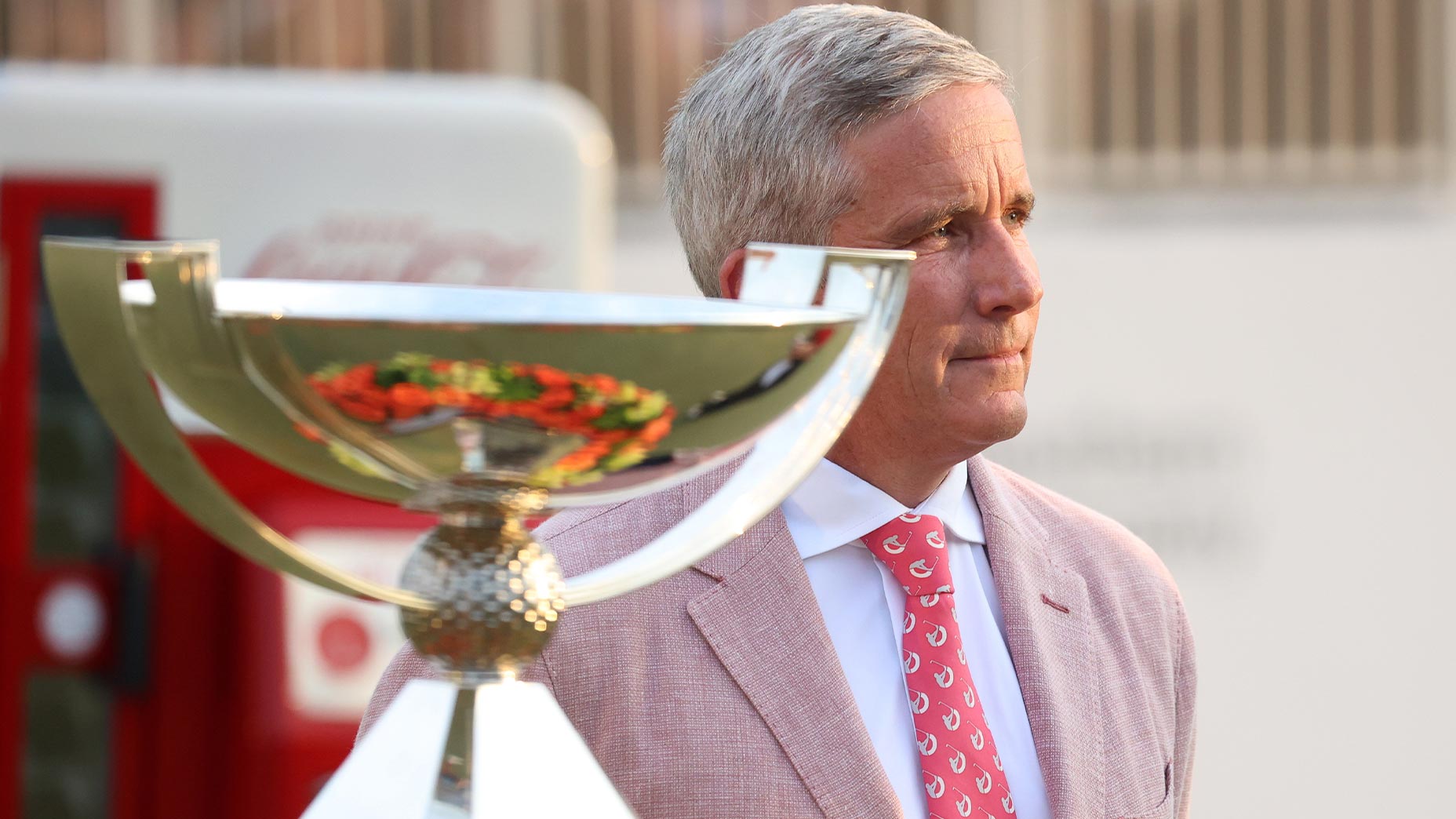 jay monahan stands in a pink suit next to fedex cup trophy