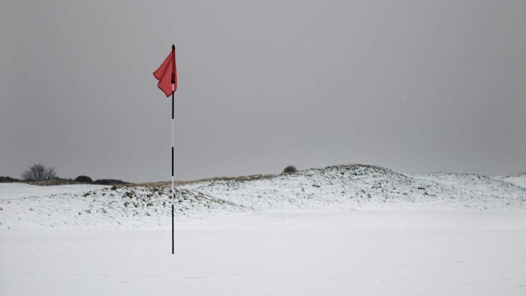 A golf flagstick on a green covered in snow.