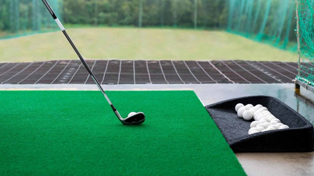 golfer sets up club behind ball on green mat with range balls next to it