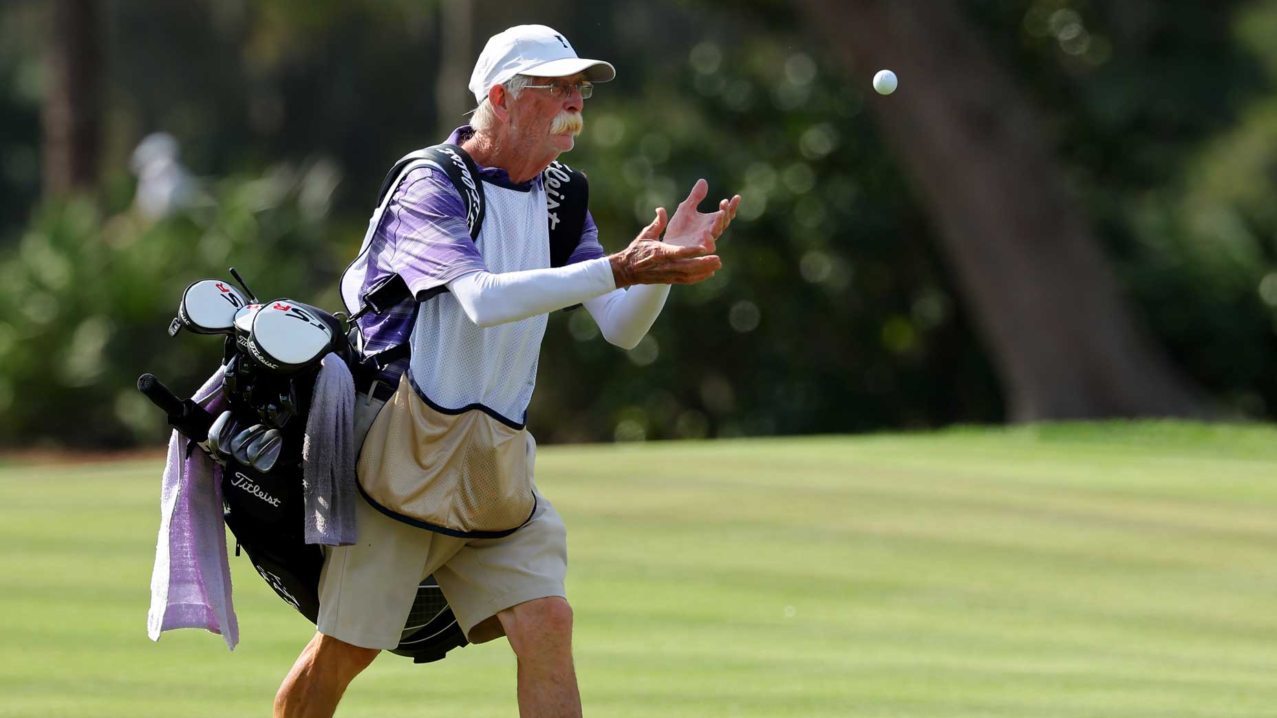 Mike "Fluff" Cowan catches a golf ball while carrying a golf bag.