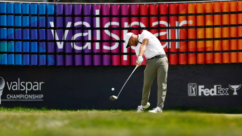 Xander Schauffele hits a driver in front of a Valspar sign.