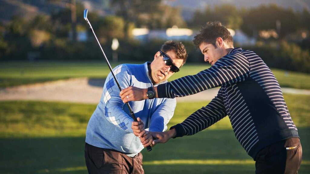 Golfer is instructed by golf teacher during swing lesson at golf course