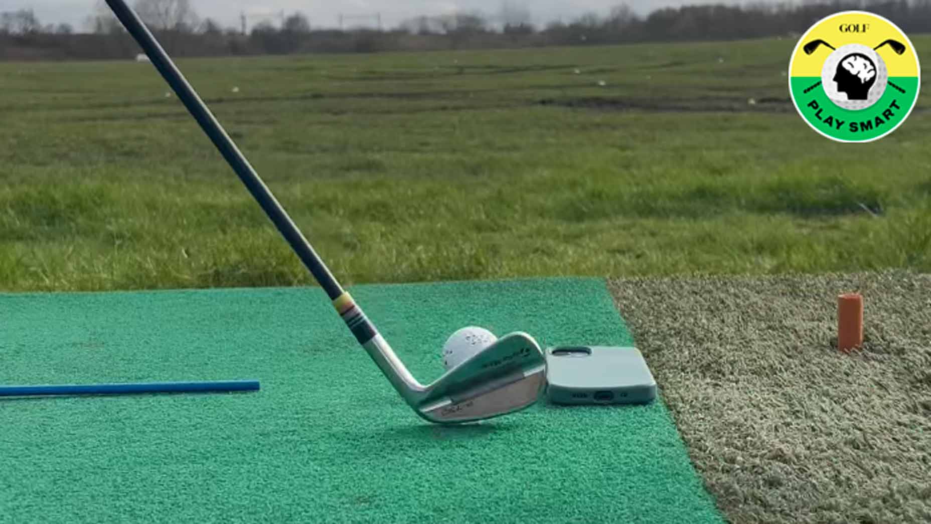 golf club lined up behind golf club with phone on ground next to it