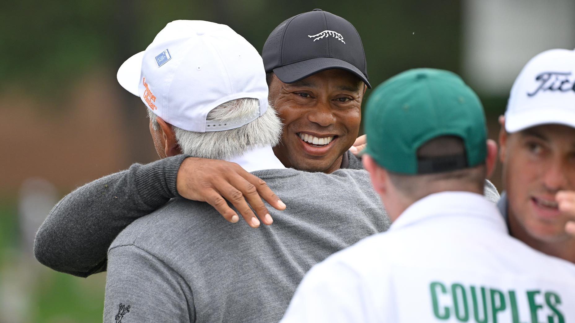 tiger woods and fred couples hug from the masters 18th green with Justin Thomas in the foreground