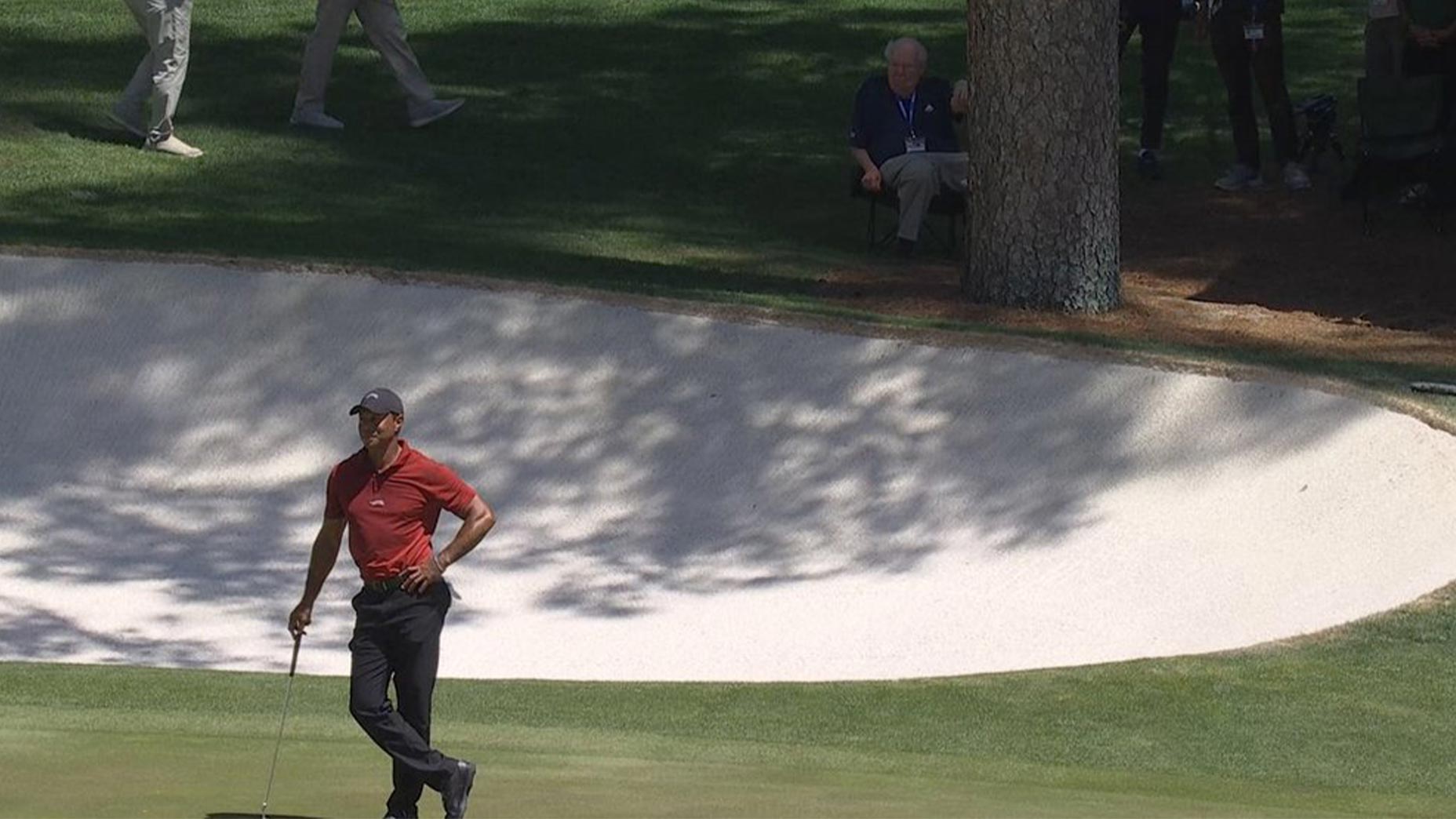 Tiger Woods stands on the 16th green of the Masters with Verne Lundquist behind him.